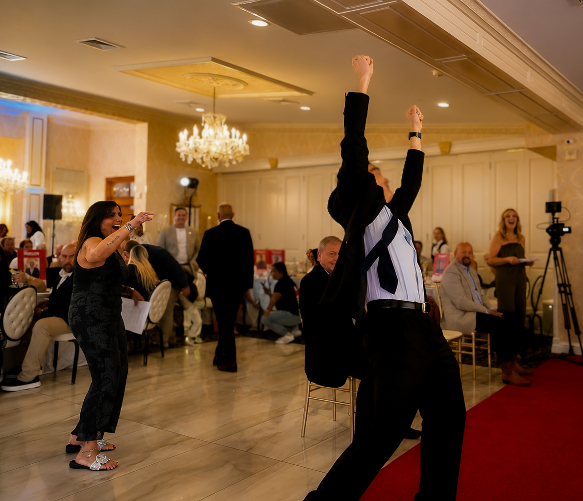 Guest cheering with both arms up on the red carpet as the room applauds