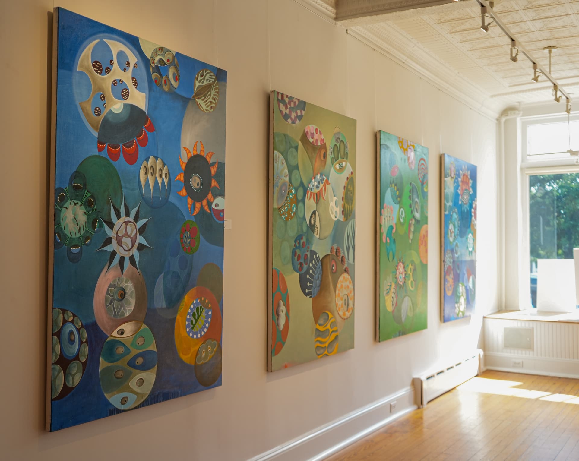 Series of vibrant abstract paintings hung along the sunlit gallery wall