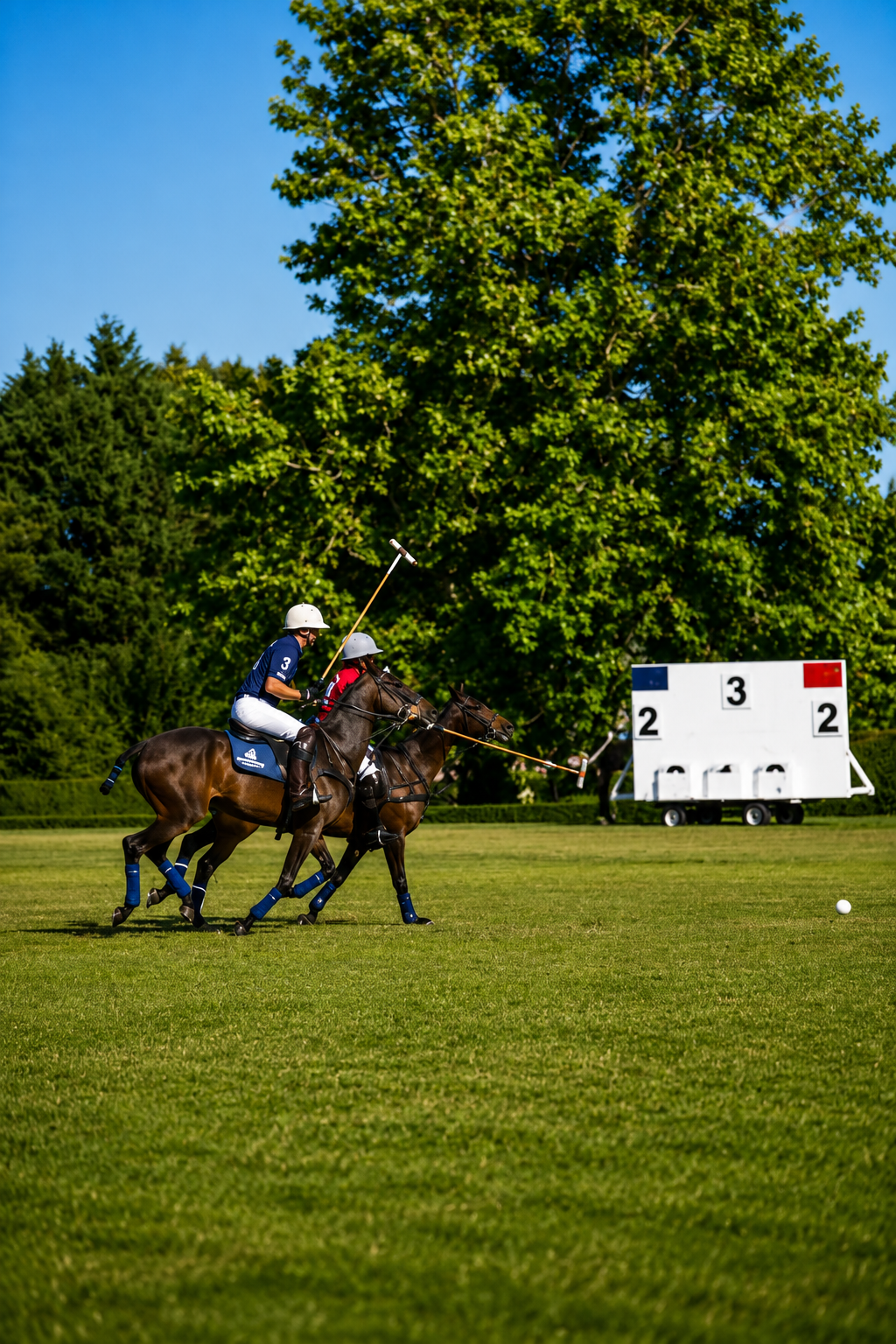 Two polo players riding the line toward the ball beside the scoreboard
