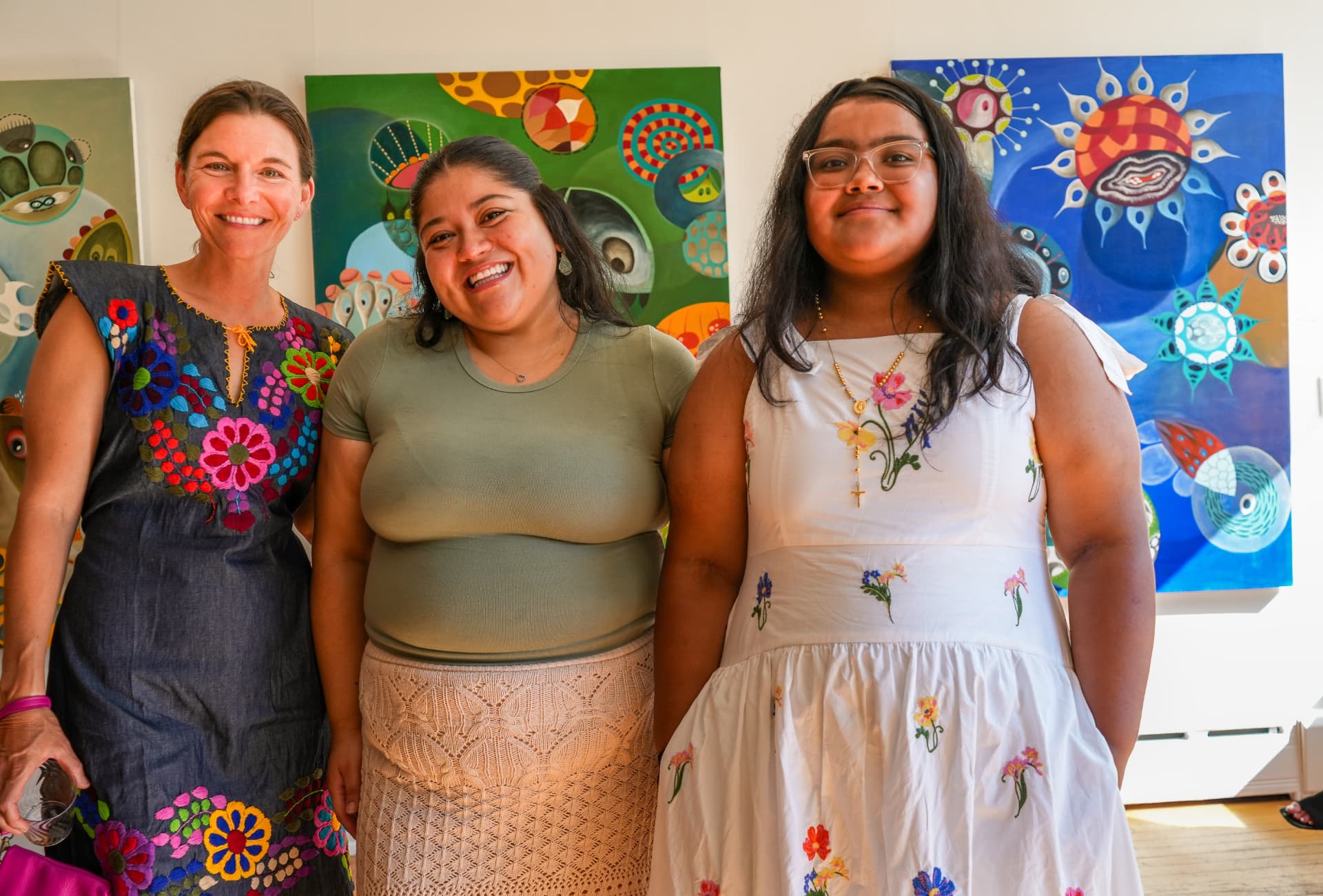 Three women smiling in front of vivid green and blue paintings