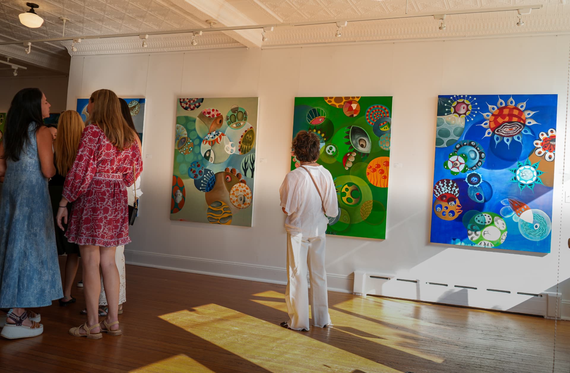 Guests viewing a row of colorful abstract paintings in the sunlit gallery