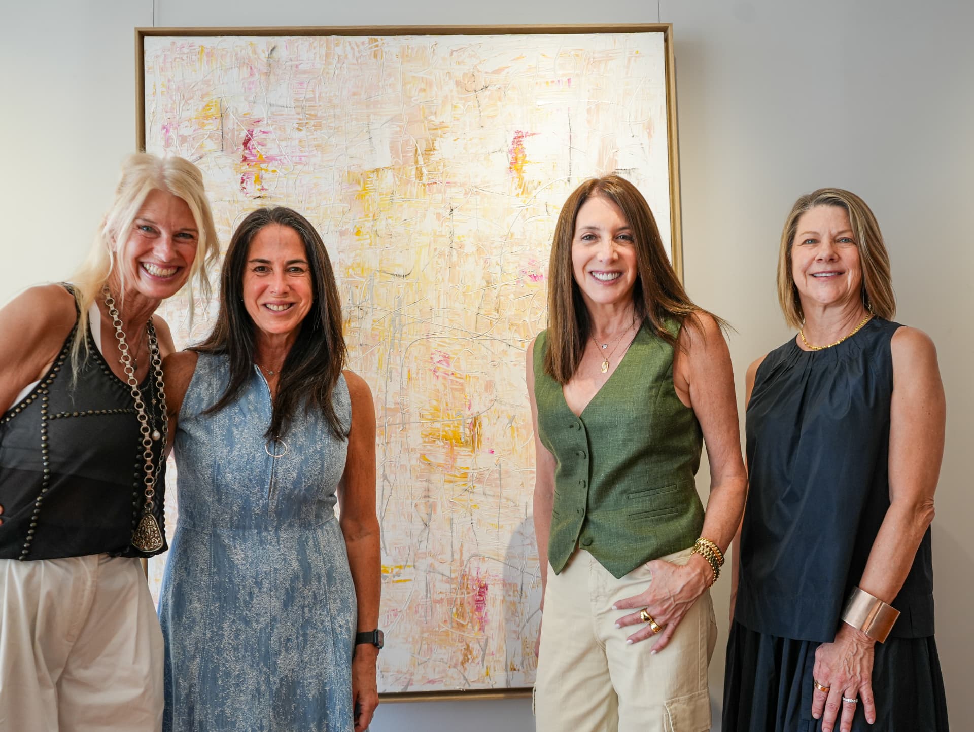 Four guests smiling together in front of a pale abstract painting