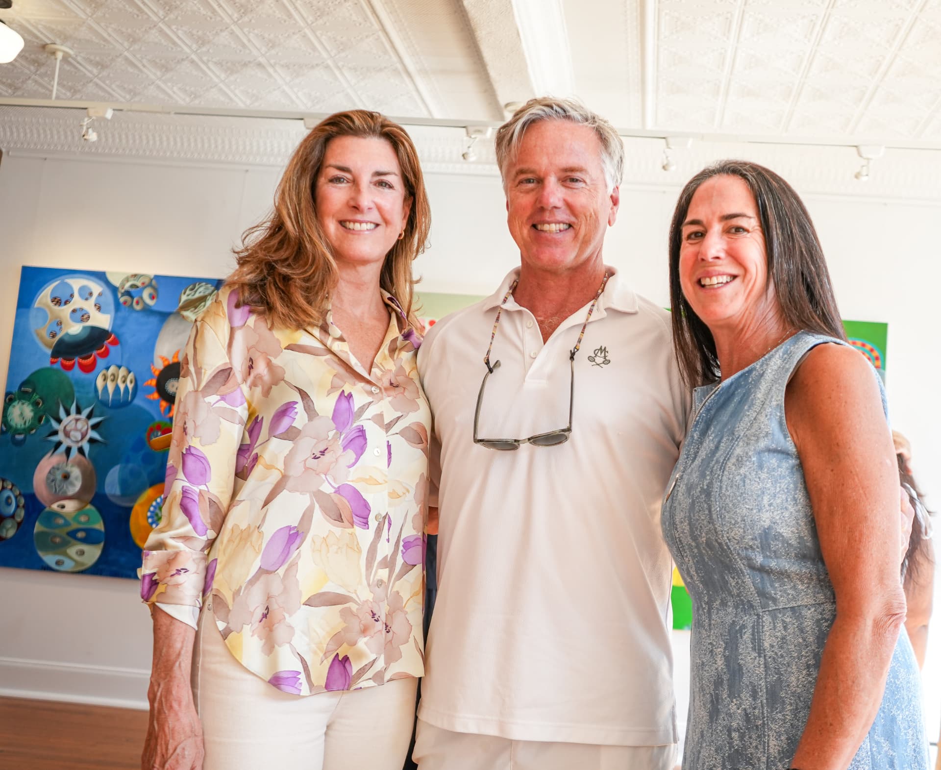 Three guests posing together in front of a blue abstract canvas