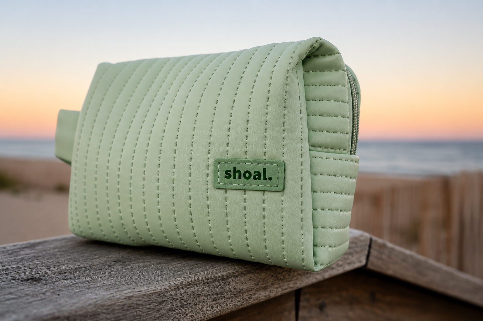 Shoal quilted travel pouch on weathered wood at dusk by the beach