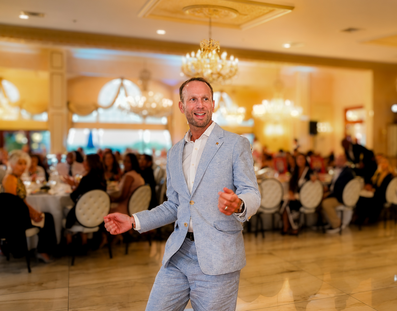 Honoree walking through the ballroom in a light linen suit as guests look on