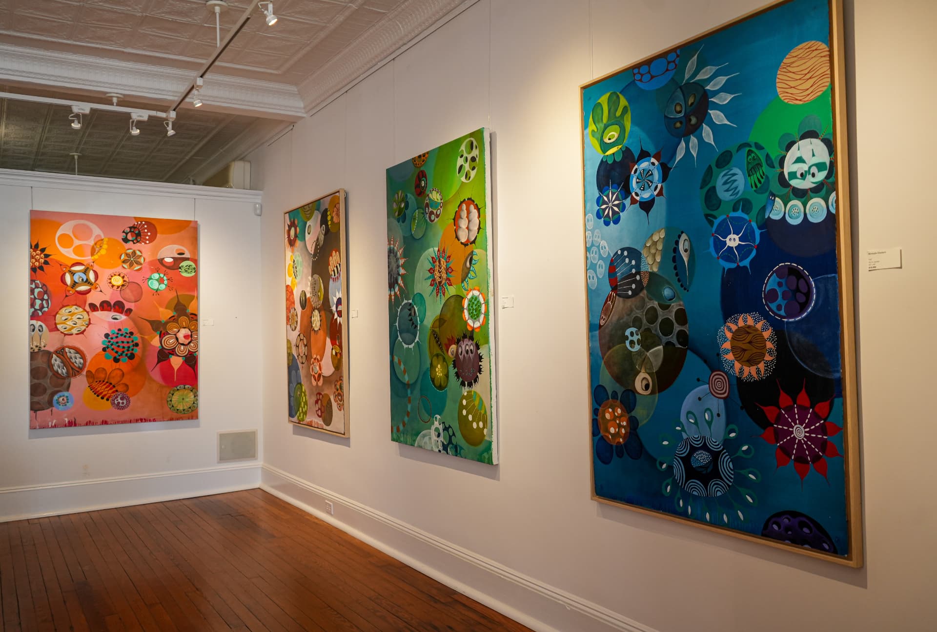 Large framed abstract canvases lining the gallery's warm wood-floored room
