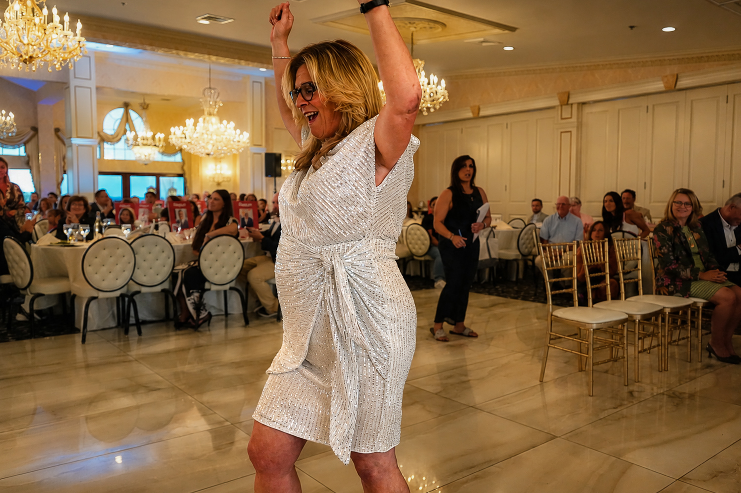 Guest in a sequined dress dancing with arms overhead in front of the seated room