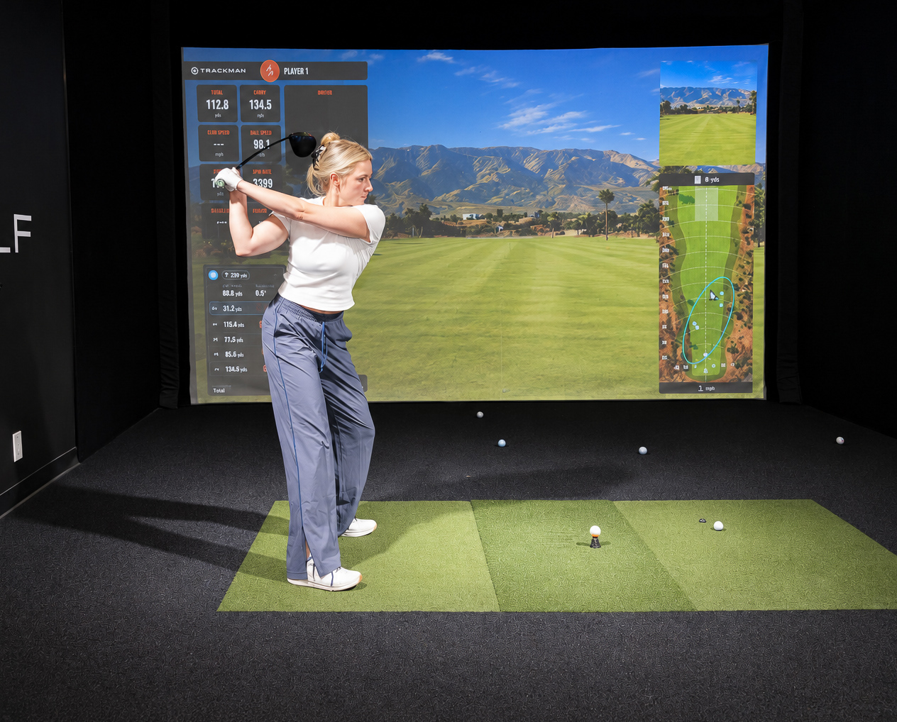 Golfer swinging in front of an indoor course simulator