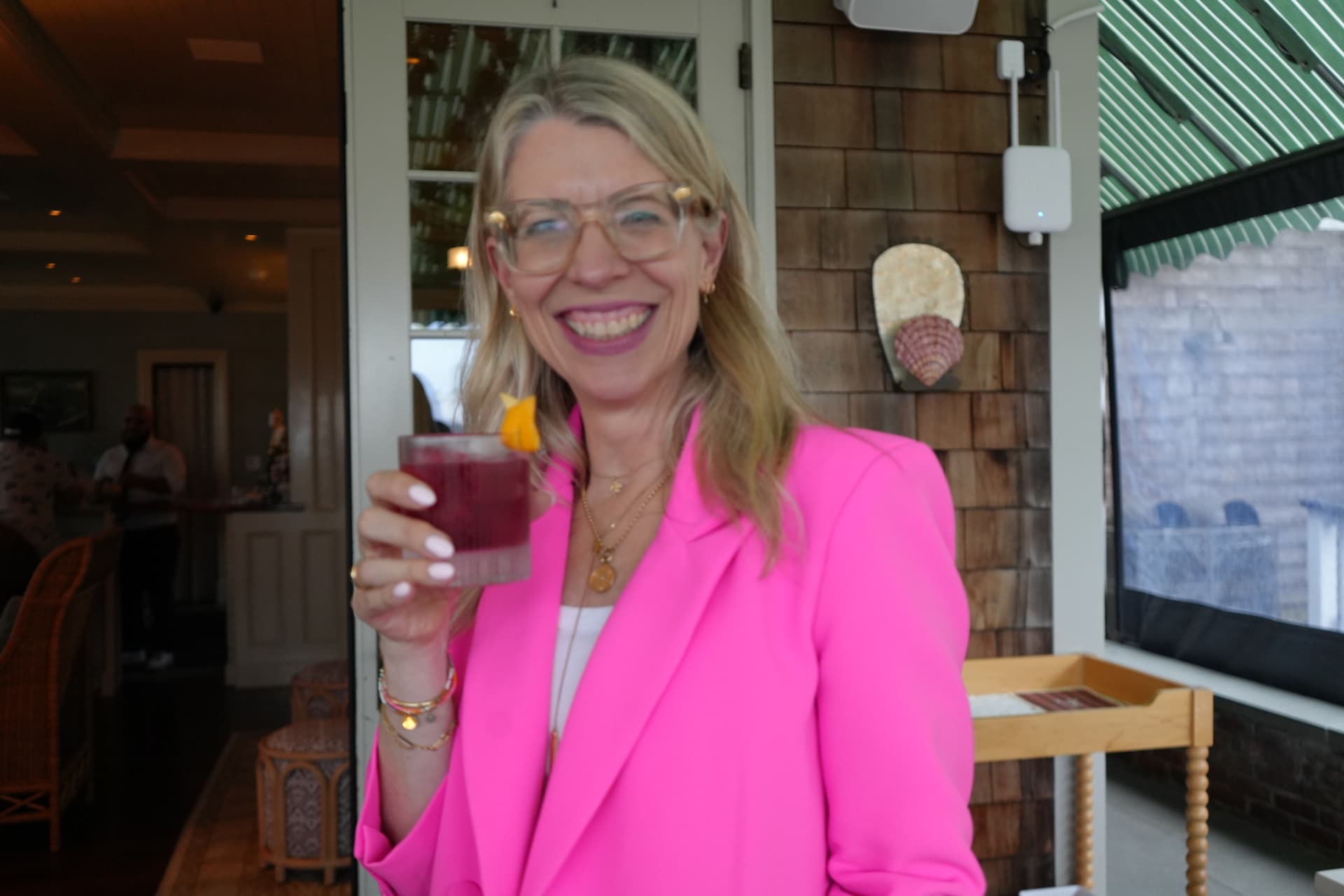 Guest in a pink blazer raising a garnished cocktail on the shingled terrace