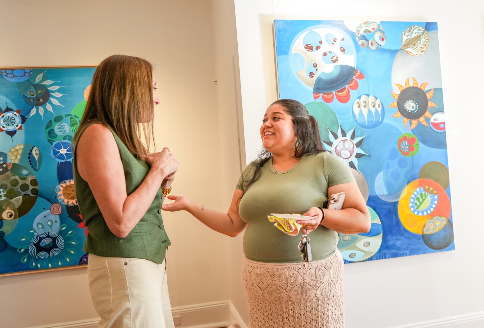Two women talking between vivid blue canvases during the reception