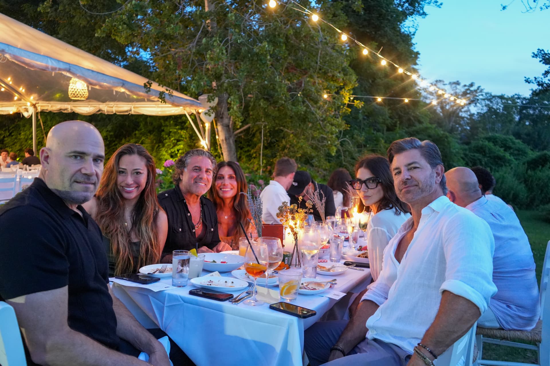 Guests turning to camera at the dinner table under string lights at dusk