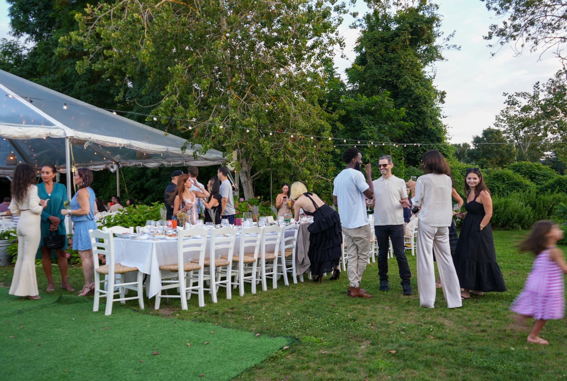 Guests arriving and mingling on the lawn beside the long white dinner table