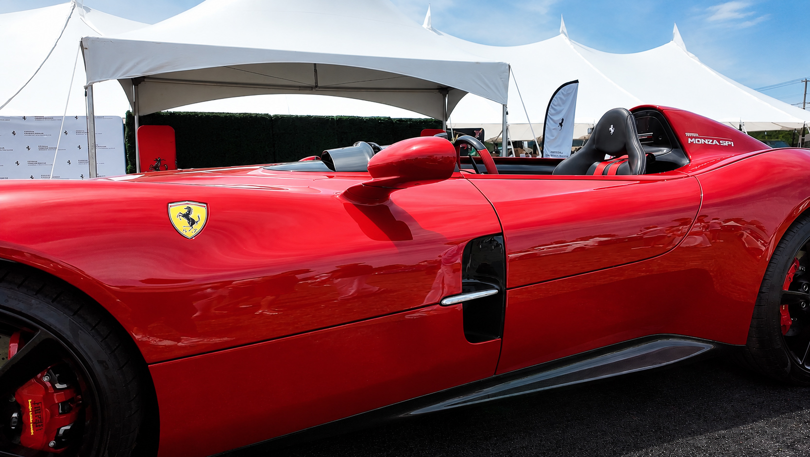 Side profile of a red Ferrari Monza SP1 beside the event tents