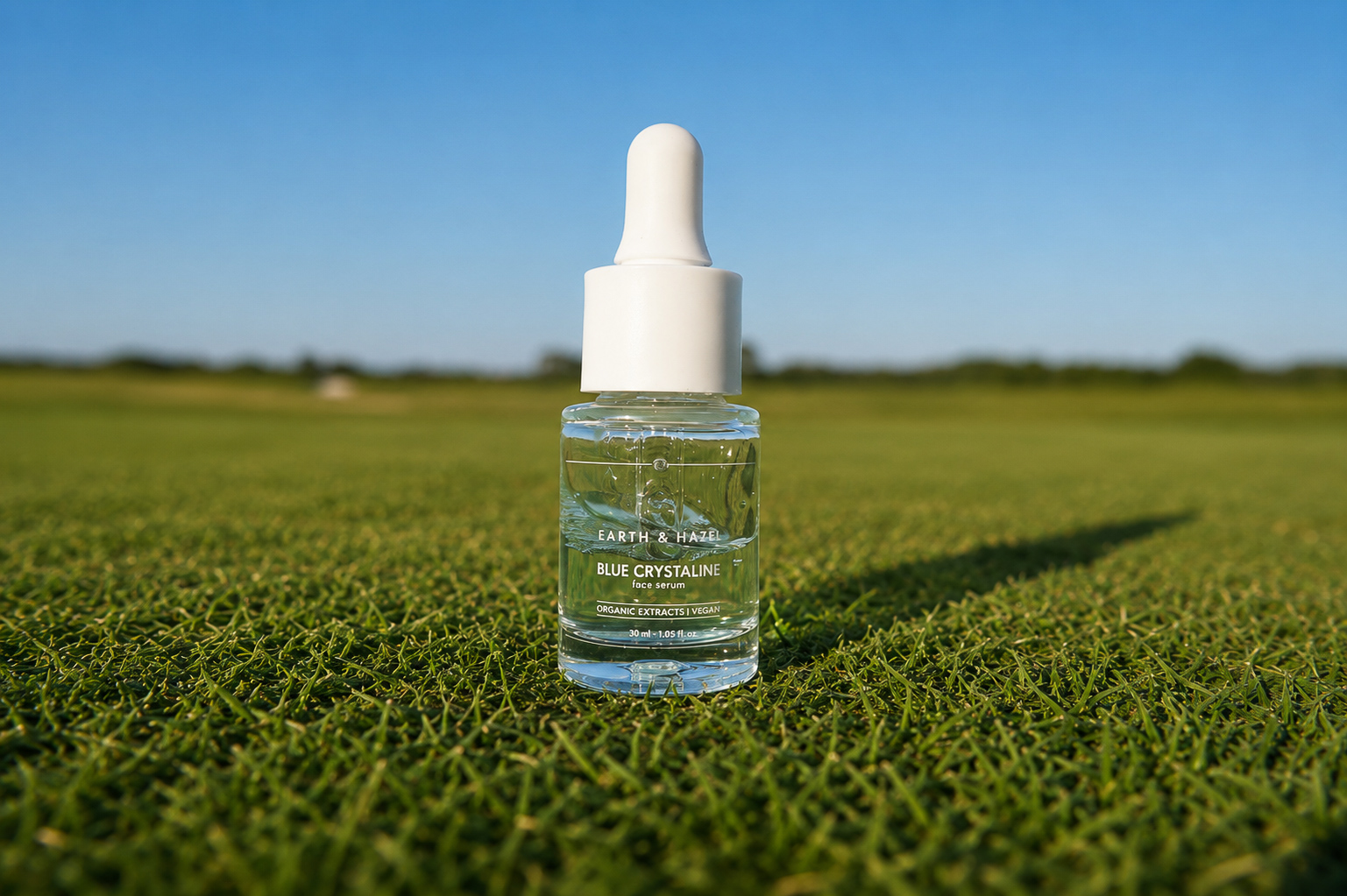 Earth & Hazel Blue Crystaline face serum on sunlit grass under a clear sky