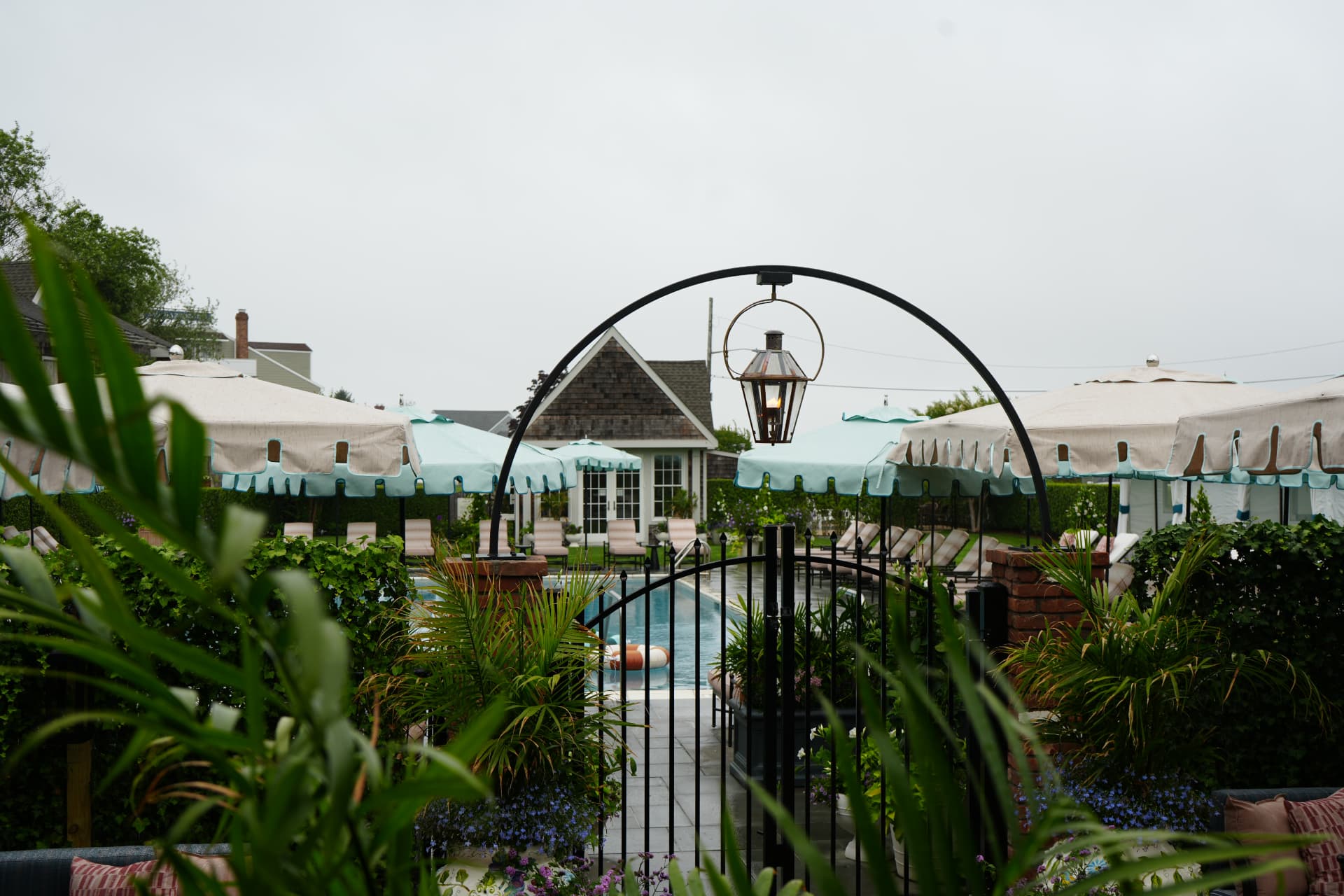 The Faraway Sag Harbor pool courtyard framed by an iron arch, lantern and striped umbrellas