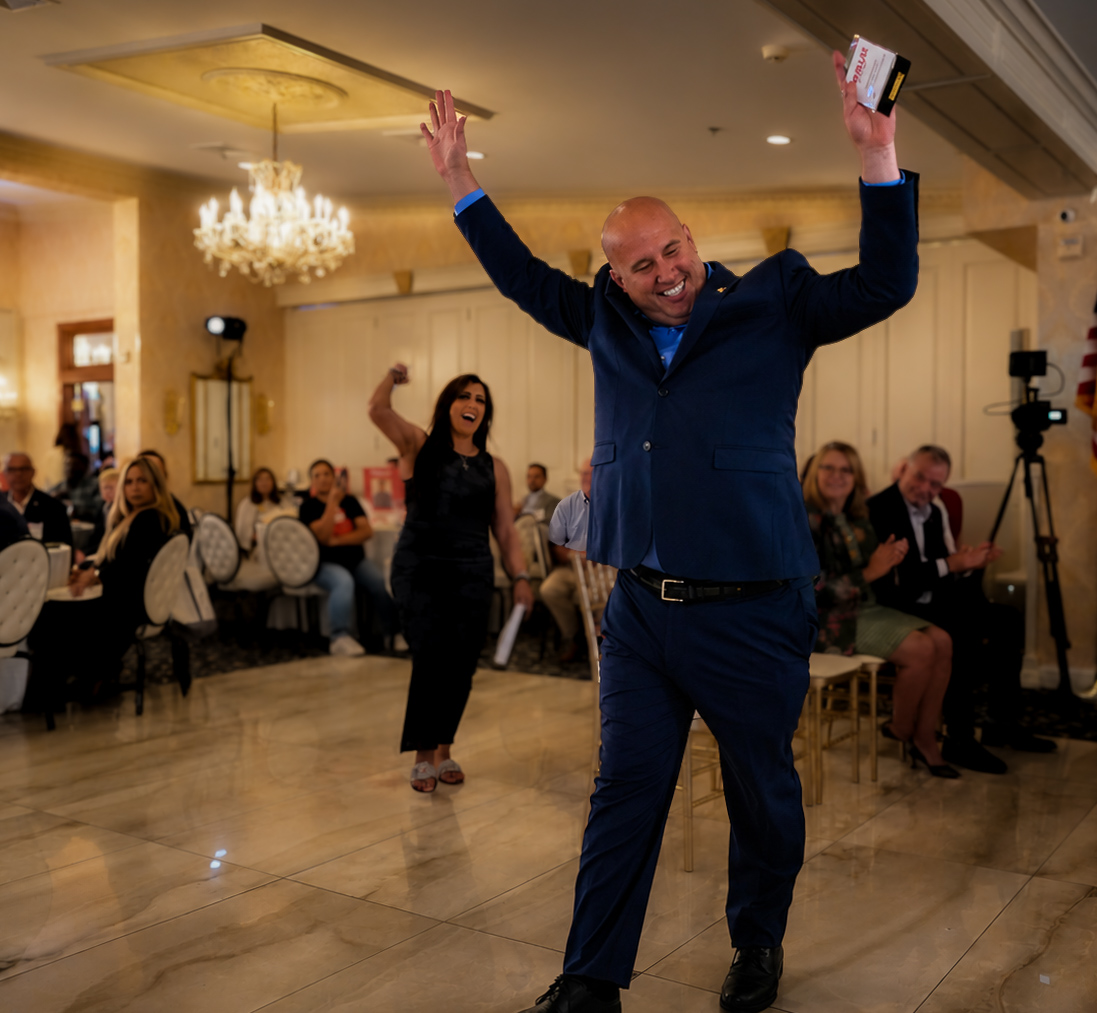 Honoree in a navy suit raising both arms in celebration as guests applaud